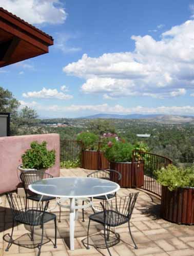 Mountain views and large metal planters with flowers located on the outside deck of a poured earth home